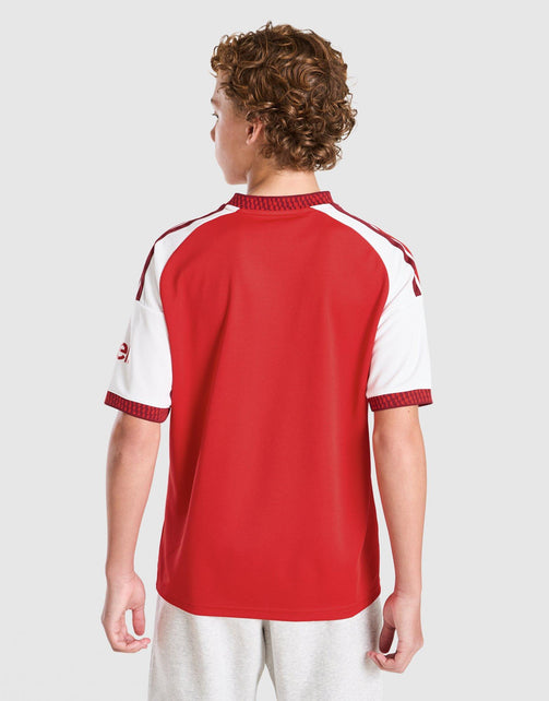 A child model shown from the back wearing adidas Arsenal FC 26/27 Home Jersey Junior's jersey with ribbed trim, paired with light gray sweatpants, against a light gray studio background.