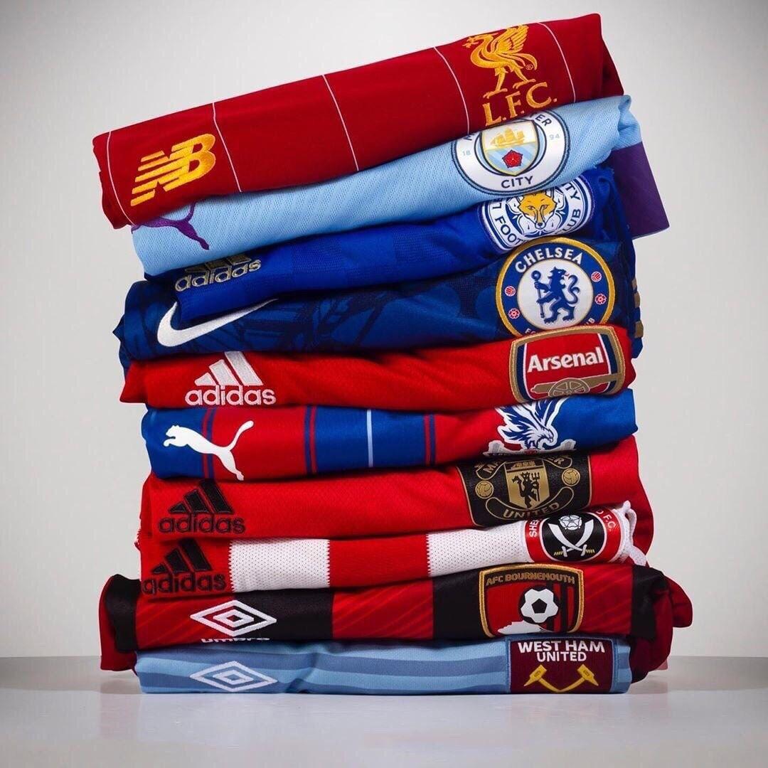A neatly stacked pile of English Premier League football jerseys showcasing team crests and brand logos, including Liverpool, Manchester City, Chelsea, Arsenal, Crystal Palace, Manchester United, Sheffield United, Bournemouth, and West Ham.