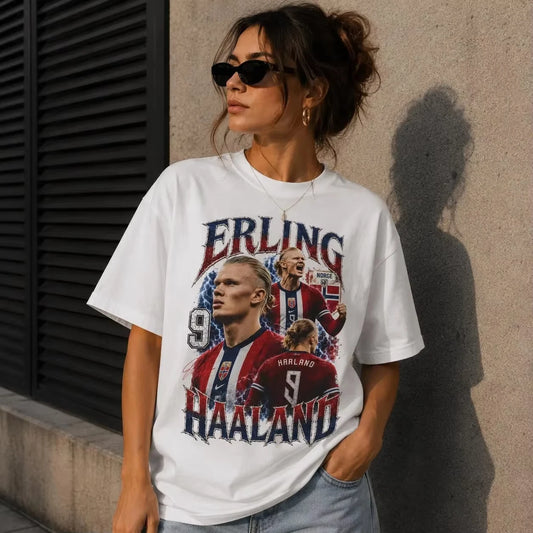 A woman wearing a white graphic t-shirt featuring Erling Haaland football player imagery, standing outdoors against a concrete wall.
