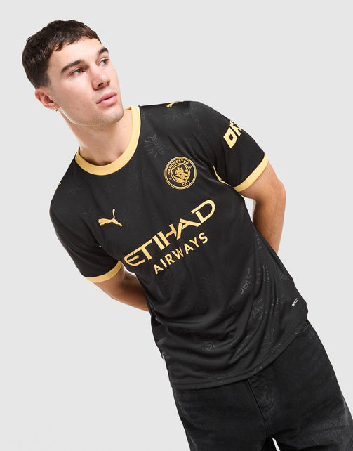 A man wearing a black Puma Etihad Airways Manchester City 2026/27 Away Jersey  with gold trim and logos, posed against a light gray background.