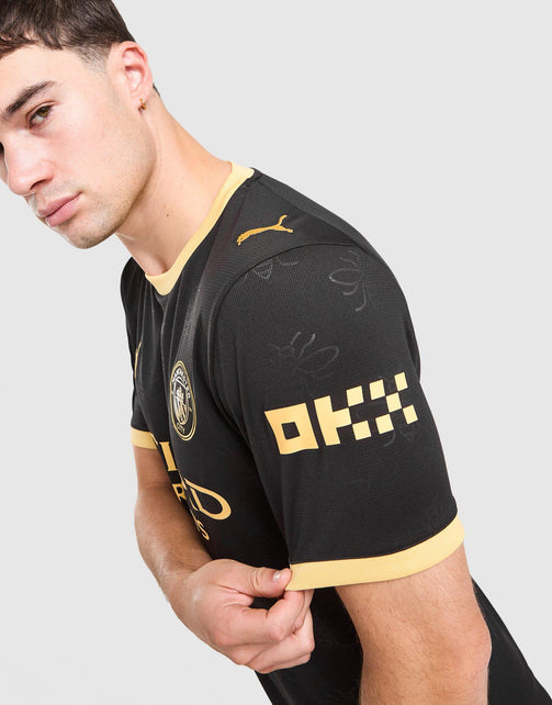 A close-up of a man wearing a black Puma Manchester City 2026/27 Away Jersey  with gold trim and a gold Puma logo, shown from the chest up against a light gray background.