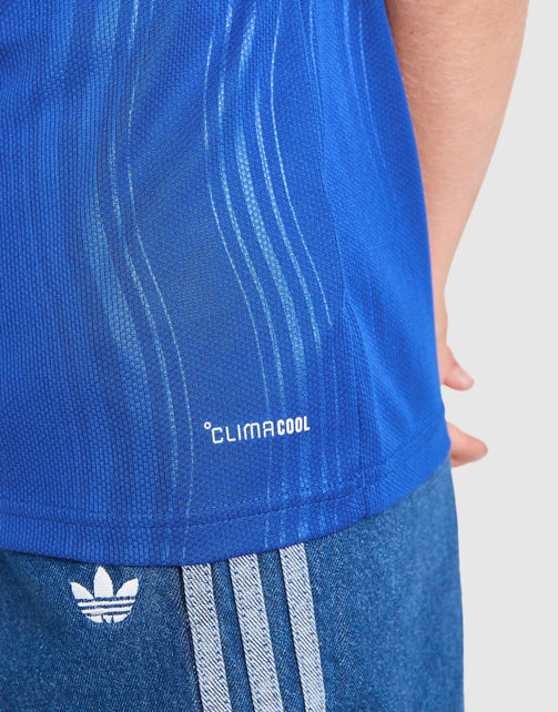 Close-up of a person wearing a bright blue Adidas Manchester United Junior 26/27 Away Jersey with 'CLIMACOOL' text and blue heathered shorts with white stripes and the Adidas trefoil logo.