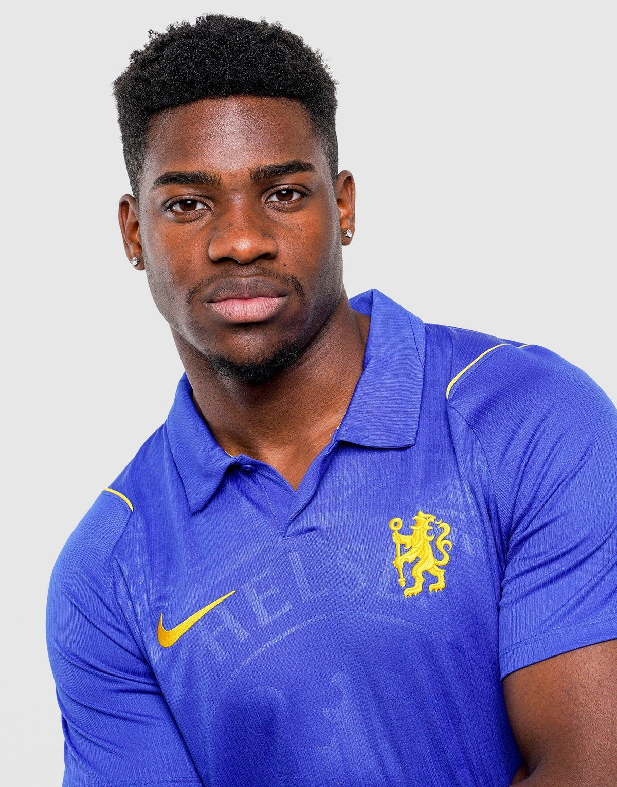 A man wearing a royal blue Nike Chelsea FC 2026/27 Home Shirt, featuring the Chelsea FC crest and a yellow Nike swoosh, posed against a light gray background.