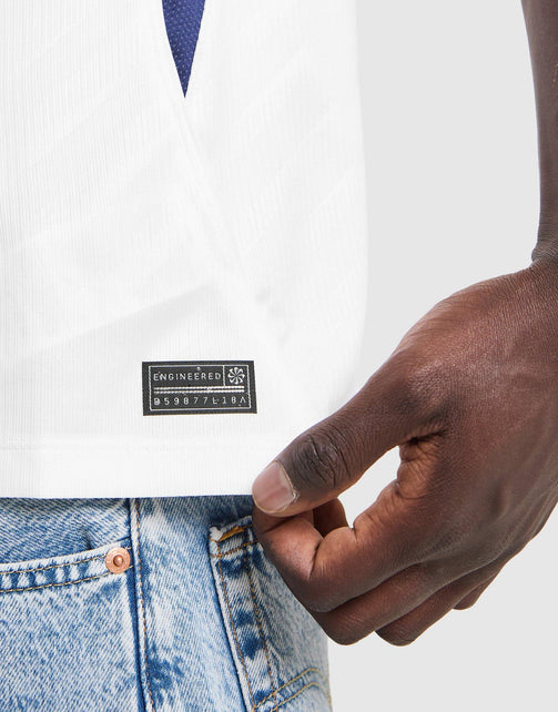 Close-up of a person wearing a white  Nike Tottenham Hotspur 2026/27 Stadium Home Dri-FIT Soccer Jersey textured jersey with a black rectangular 'ENGINEERED' brand patch on the chest, paired with light blue jeans.