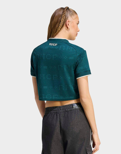 A woman shown from the back wearing a Real Madrid 26/27 Cropped Fan Jersey dark teal cropped short-sleeve polo shirt with a subtle tonal pattern and white trim, paired with dark gray pants, against a light gray studio background.