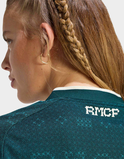 Close-up side profile of a woman wearing a Real Madrid 26/27 Cropped Fan Jersey with white 'RMCF' lettering on the back, shown against a light gray background.