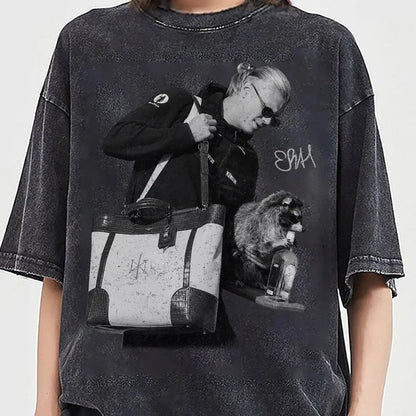 Erling Haaland  wearing an oversized black acid-wash graphic t-shirt featuring a monochrome print of a man carrying a tote bag and a raccoon holding a bottle. The t-shirt has a distressed, faded black finish with raw hems.