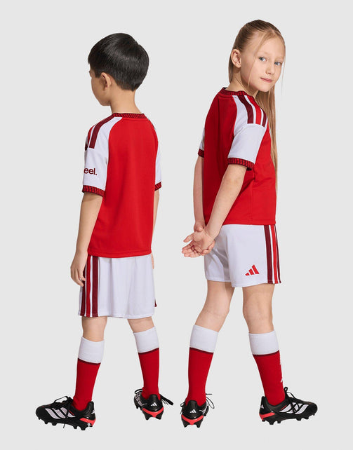 Two children modeling a red and white adidas Arsenal FC 26/27 Home Set Children's soccer kit, showing both front and back views against a light gray background.