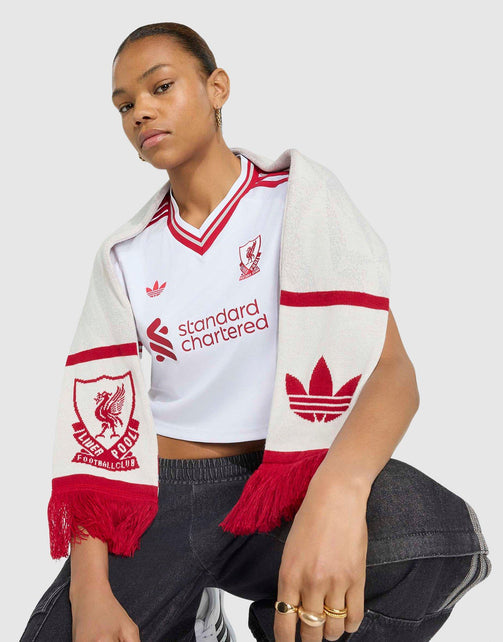 A model wearing a white adidas Liverpool FC 26/27 Away Jersey Crop jersey with red trim and a matching white and red Adidas scarf draped over her shoulders, posed against a light gray studio background.