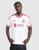 A man modeling a white adidas Liverpool FC 26/27 Away Jersey with red stripes and logos, including the standard chartered sponsor logo, against a light gray background.