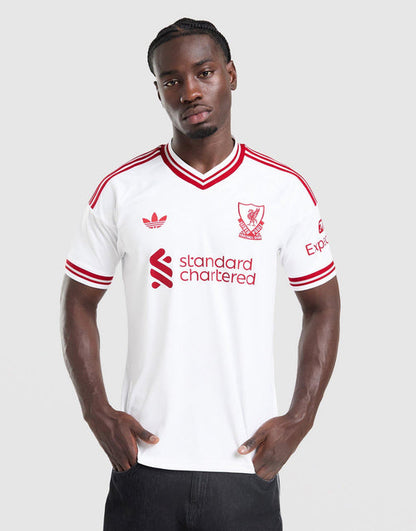 A man modeling a white adidas Liverpool FC 26/27 Away Jersey with red stripes and logos, including the standard chartered sponsor logo, against a light gray background.