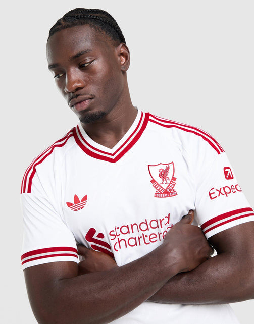 A man wearing a white adidas Liverpool FC 26/27 Away Jersey with red stripes and logos, posed against a light gray studio background.