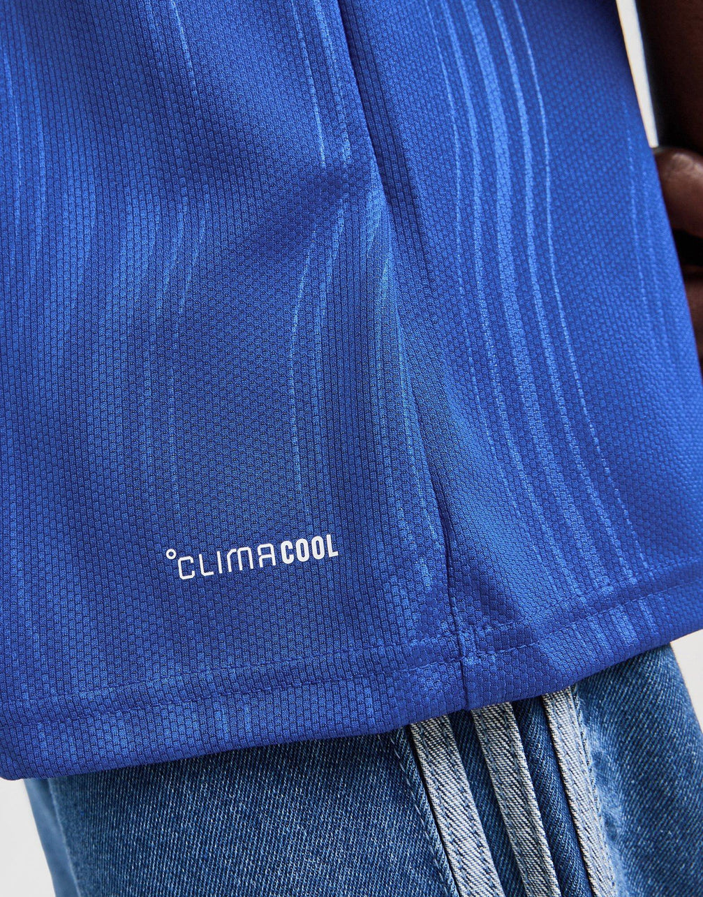 Close-up of a blue adidas Manchester United 26/27 Away Jersey with the 'CLIMACOOL' logo printed in white near the hem, worn over blue jeans.